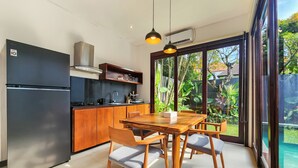 A modern kitchen with a refrigerator, stove, and wooden cabinets. There is a dining area with a table and chairs. - Villa Movida Canggu by Nagisa Bali (Kerobokan)