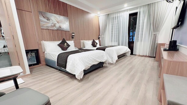 A hotel room with two beds, a desk, a chair, a TV, and a large window with curtains. - One Villa Hotel 6 (Hanoi)