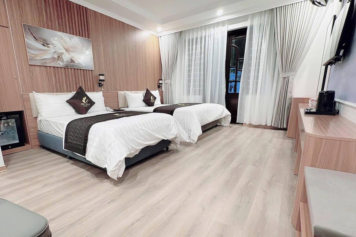 A hotel room with two beds, a desk, a chair, a TV, and a large window with curtains.