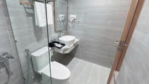 A modern bathroom with a glass shower enclosure, a toilet, a sink with a vanity, and a towel rack. - One Villa Hotel 6 (Hanoi)