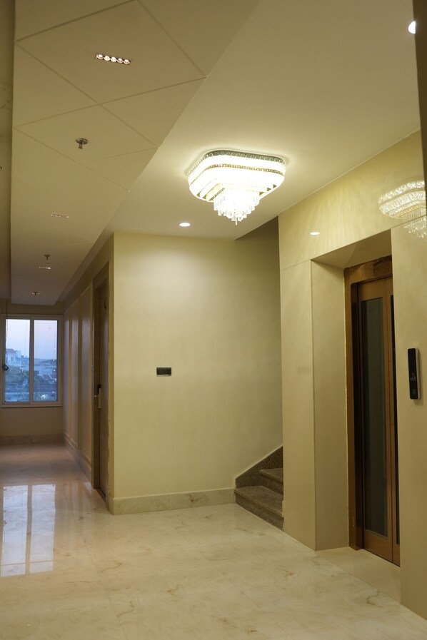 A hallway with a marble floor, a staircase, and a door with a modern light fixture above it. - Hotel Green Palace (Prayagraj)