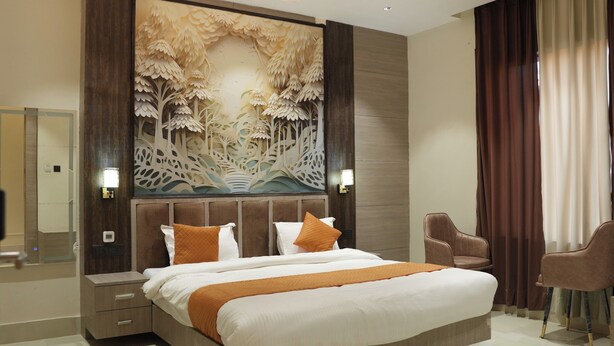 A modern hotel room with a large bed, a nightstand, a chair, and a decorative wall panel. - Hotel Green Palace (Prayagraj)