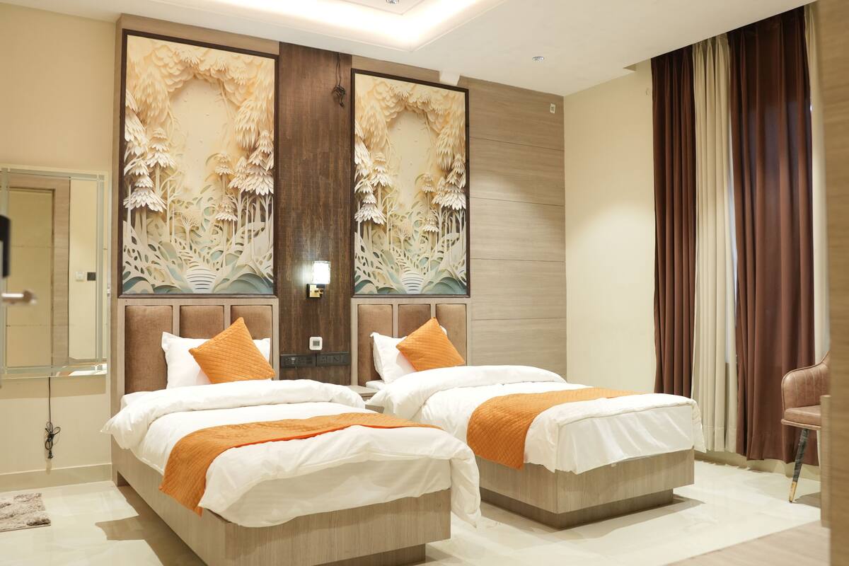 Habitación de hotel con dos camas, un panel decorativo grande, un espejo y una ventana con cortinas.