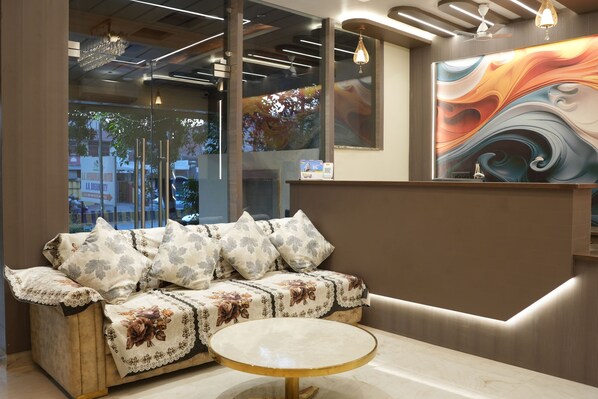 A modern interior with a sofa, a round table, and a colorful abstract painting. - Hotel Green Palace (Prayagraj)