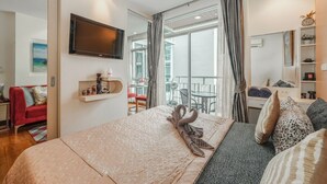 Habitación de hotel con cama, televisión, balcón con mesa y sillas, y vistas al exterior.
