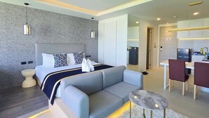 Un dormitorio moderno con cama, mesitas de noche, sofá, zona de comedor con sillas y cocina.
