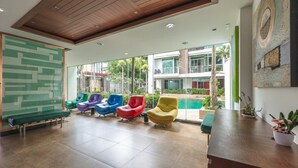 Un vestíbulo moderno con sillas coloridas, un mostrador de recepción y vistas a una piscina y edificios.