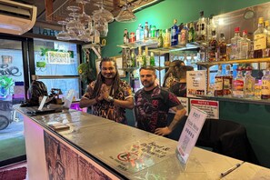 Un espace bar avec des étagères remplies de bouteilles d’alcool, un comptoir avec un menu et un panneau indiquant les différents types de boissons et leurs prix.