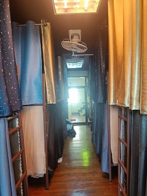 Ein schmaler Korridor mit Holzboden, Deckenventilator und Vorhängen an beiden Seiten.