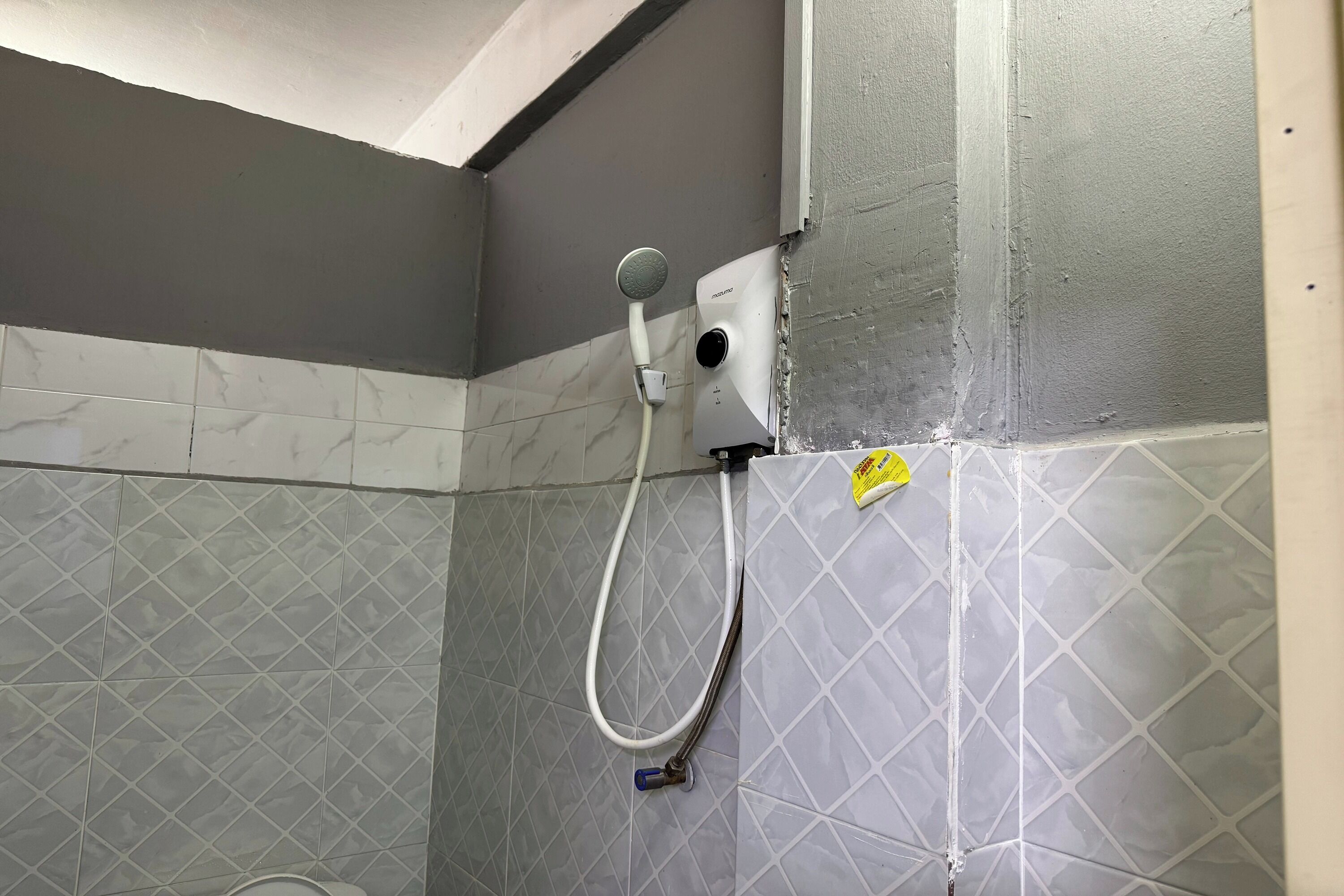 A shower area with a handheld showerhead, a wall-mounted control panel, and a yellow warning sticker on the wall.