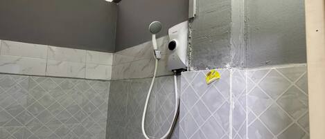 A shower area with a handheld showerhead, a wall-mounted control panel, and a yellow warning sticker on the wall.