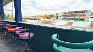 Un bar situé sur un toit, avec des tabourets de bar aux couleurs vives et une vue sur les bâtiments en arrière-plan.
