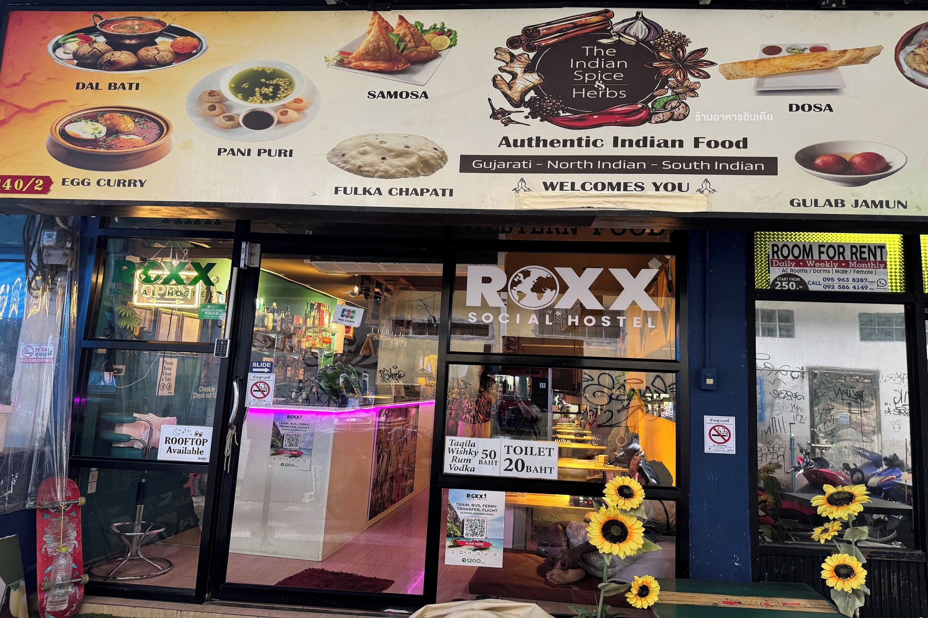 A social hostel with a menu board advertising Indian food, a sign for room rent, and a visible toilet sign.