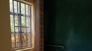 Een hotelkamer met een bed, een raam met tralies, een donkergroene muur en een handdoek op het bed.