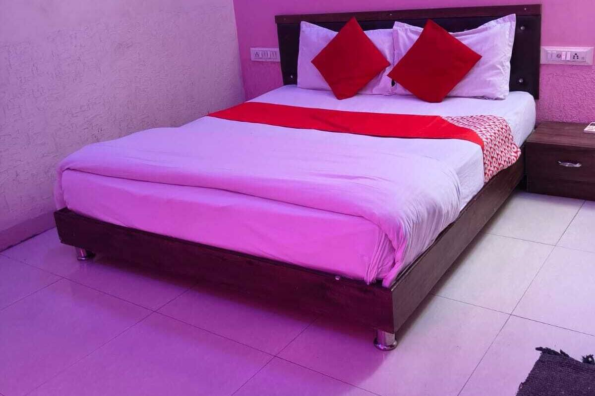 A neatly made bed with a red and white bedspread, two red pillows, and a wooden headboard.