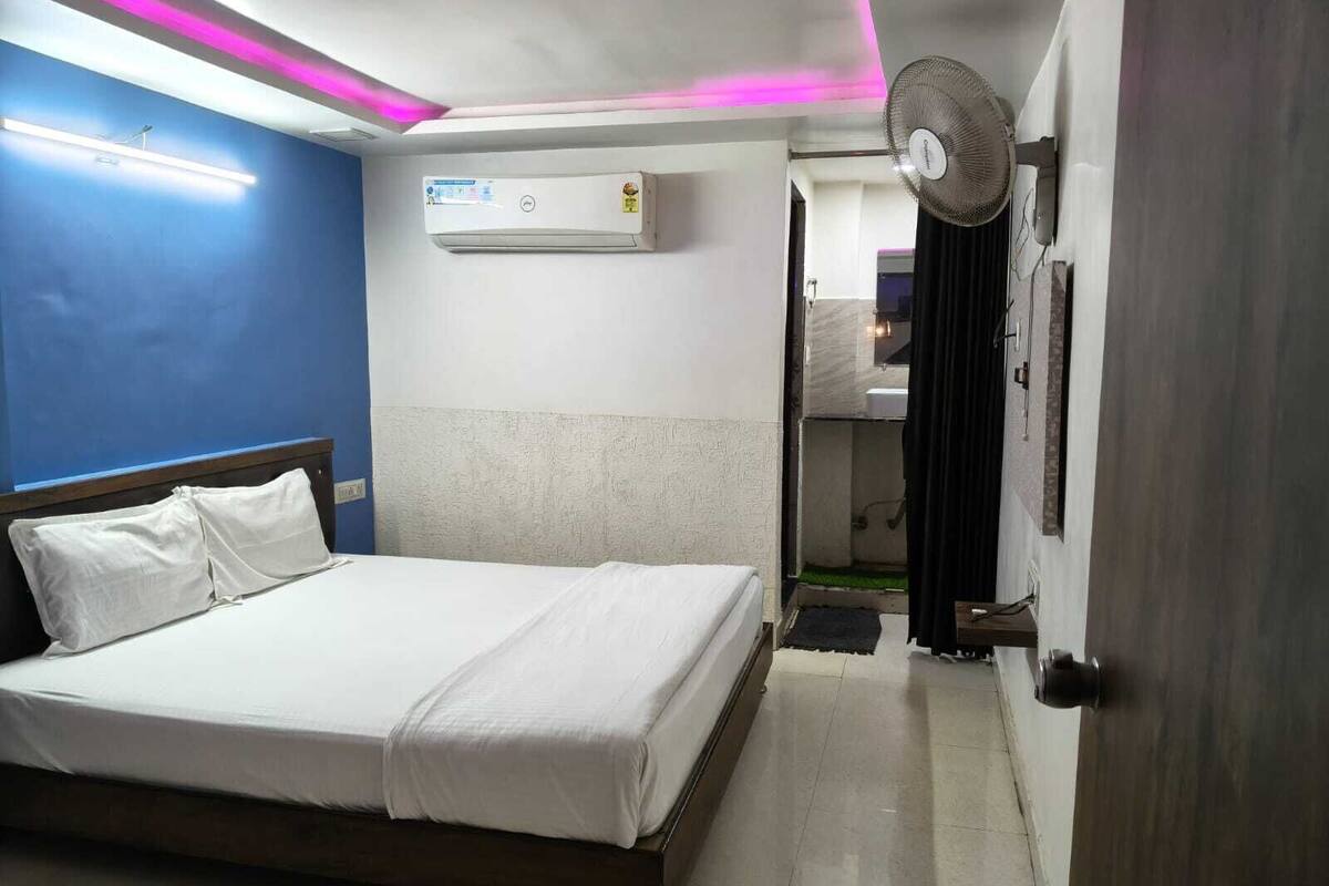 A hotel room with a bed, an air conditioner, a ceiling fan, and a door leading to a bathroom.