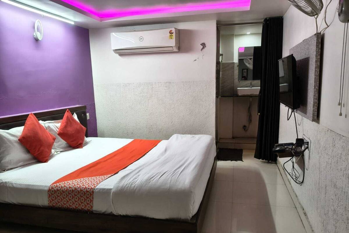 A hotel room with a bed, a TV, an air conditioning unit, and a bathroom visible through an open door.