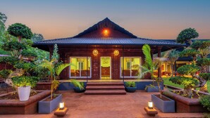 A building with a tiled roof, large windows, and a well-maintained garden with various plants and a pathway leading to the entrance. - Zo Selections Gokarna by Zostel (Gokarna)