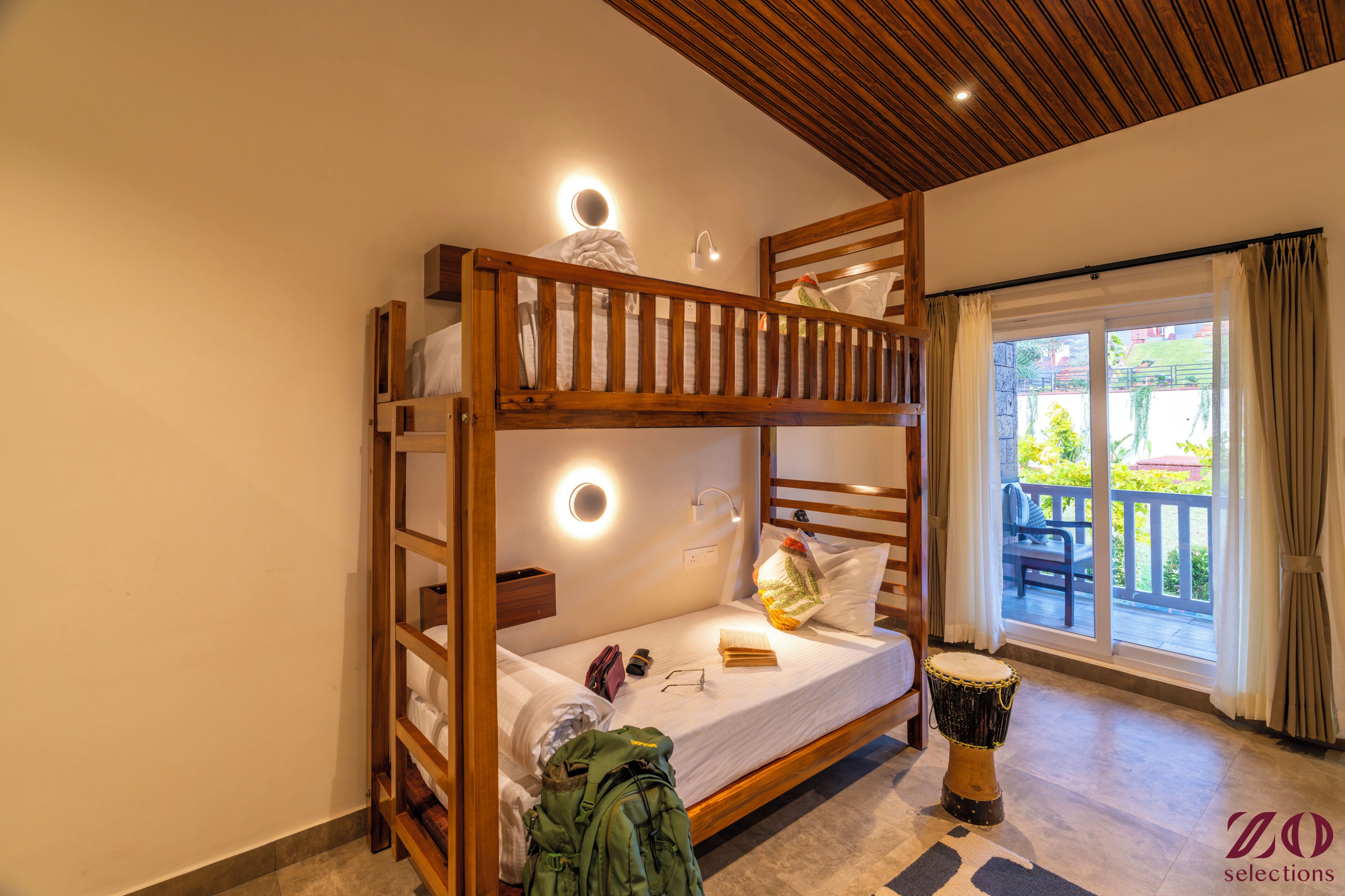 Un lit superposé avec une structure en bois, une table de chevet avec une lampe, une batterie et une fenêtre avec des rideaux.
