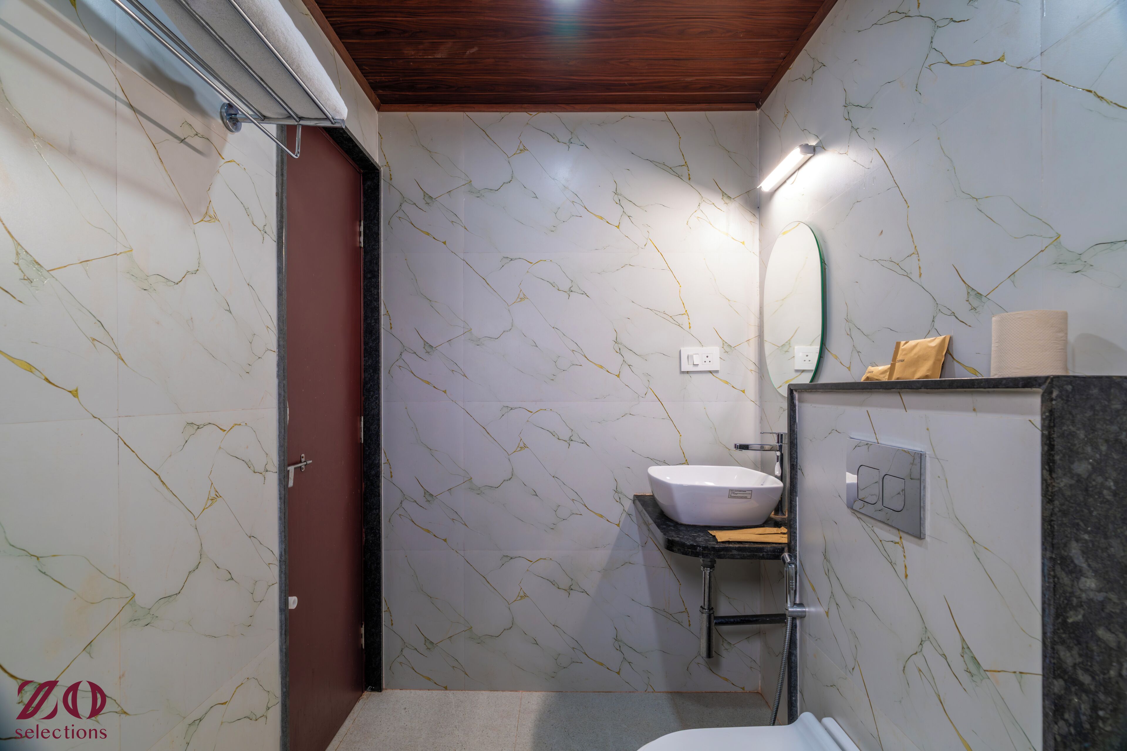 A bathroom with a marble wall, a sink, a mirror, and a towel rack.