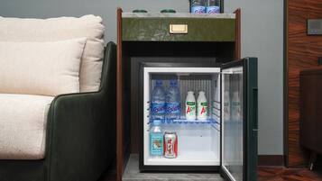 Un refrigerador compacto con compartimento congelador, que contiene agua embotellada y una lata de refresco.