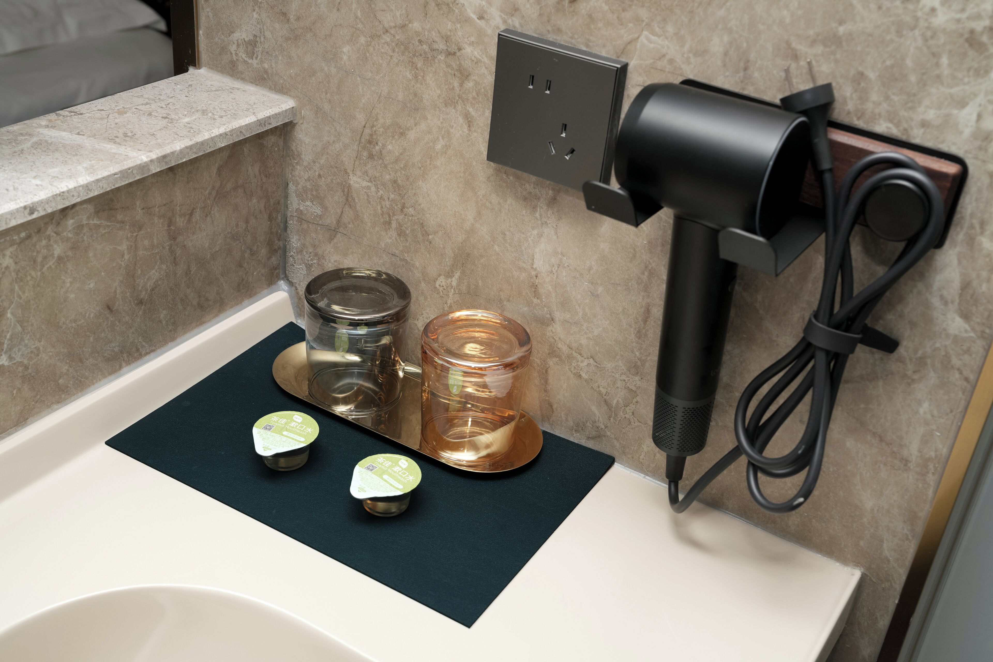 A bathroom with a sink, a hairdryer, and two containers on a mat.