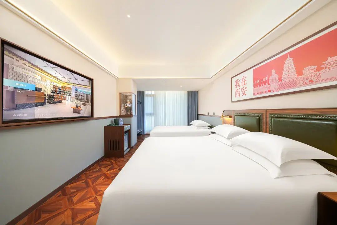 A hotel room with two beds, a desk, a chair, a TV, and a framed picture on the wall.