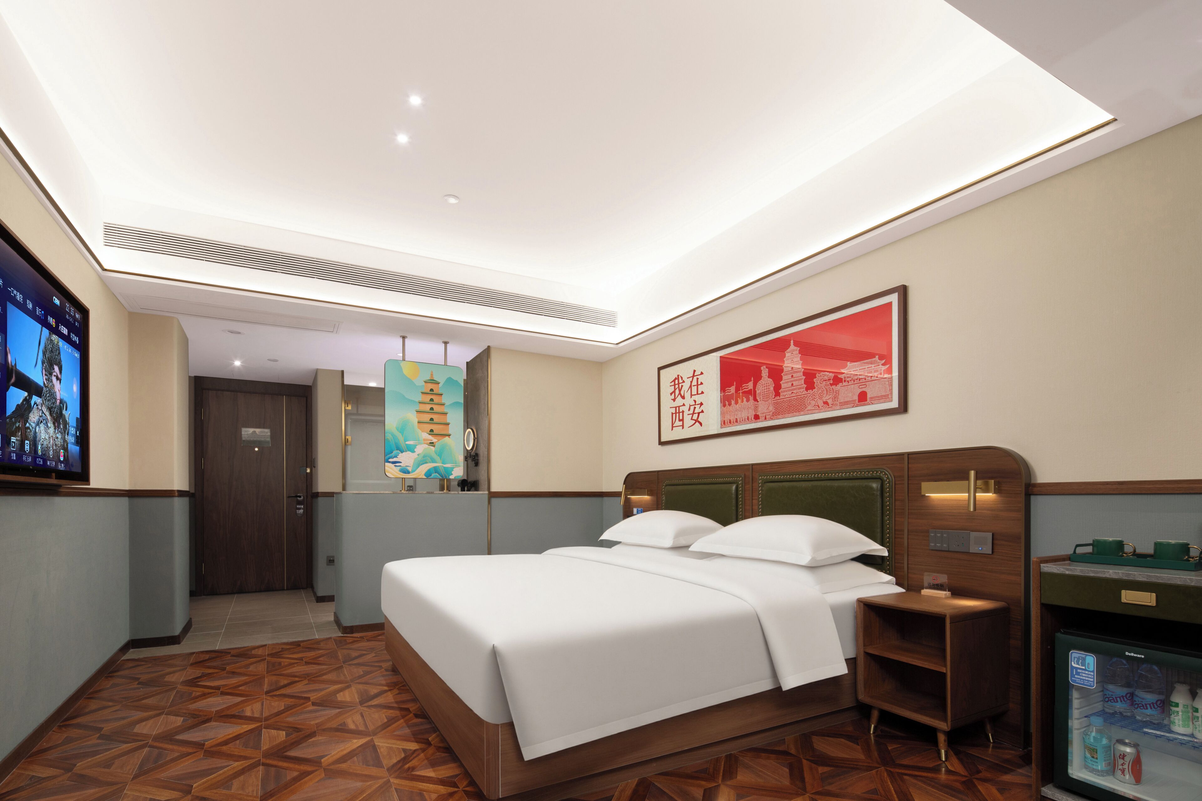 A hotel room with a bed, a nightstand, a minibar, a television, and a painting on the wall.