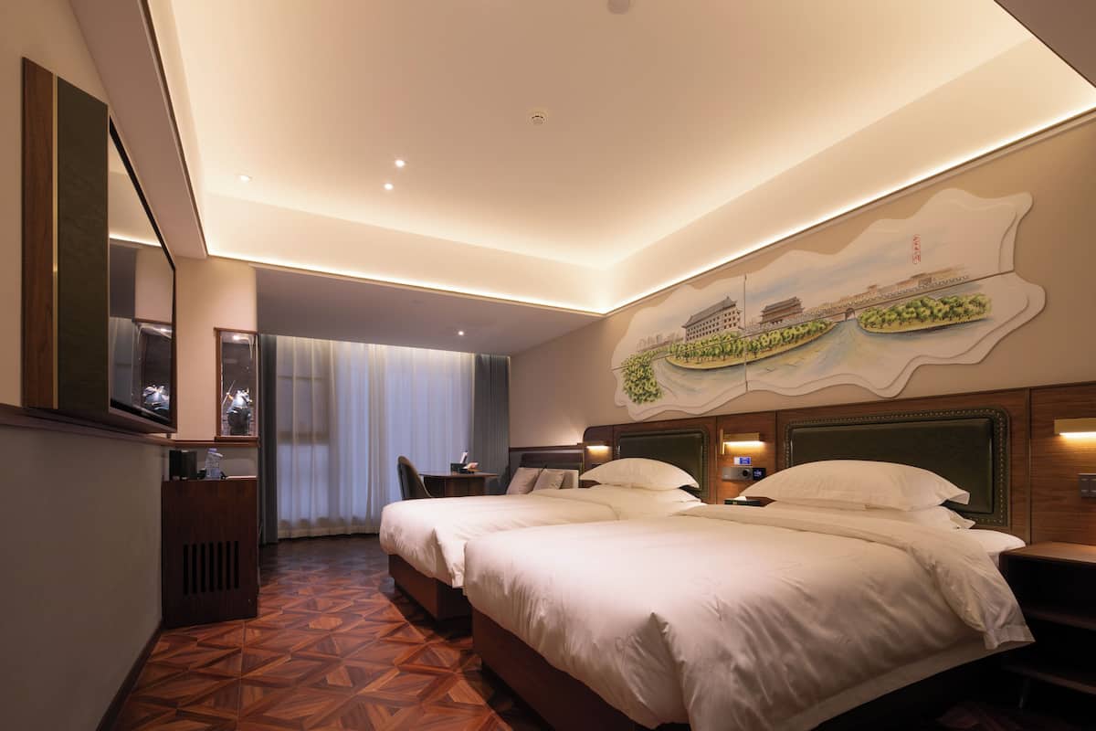 Ein Hotelzimmer mit zwei Betten, einem großen Spiegel, Wandgemälde und Holzboden.