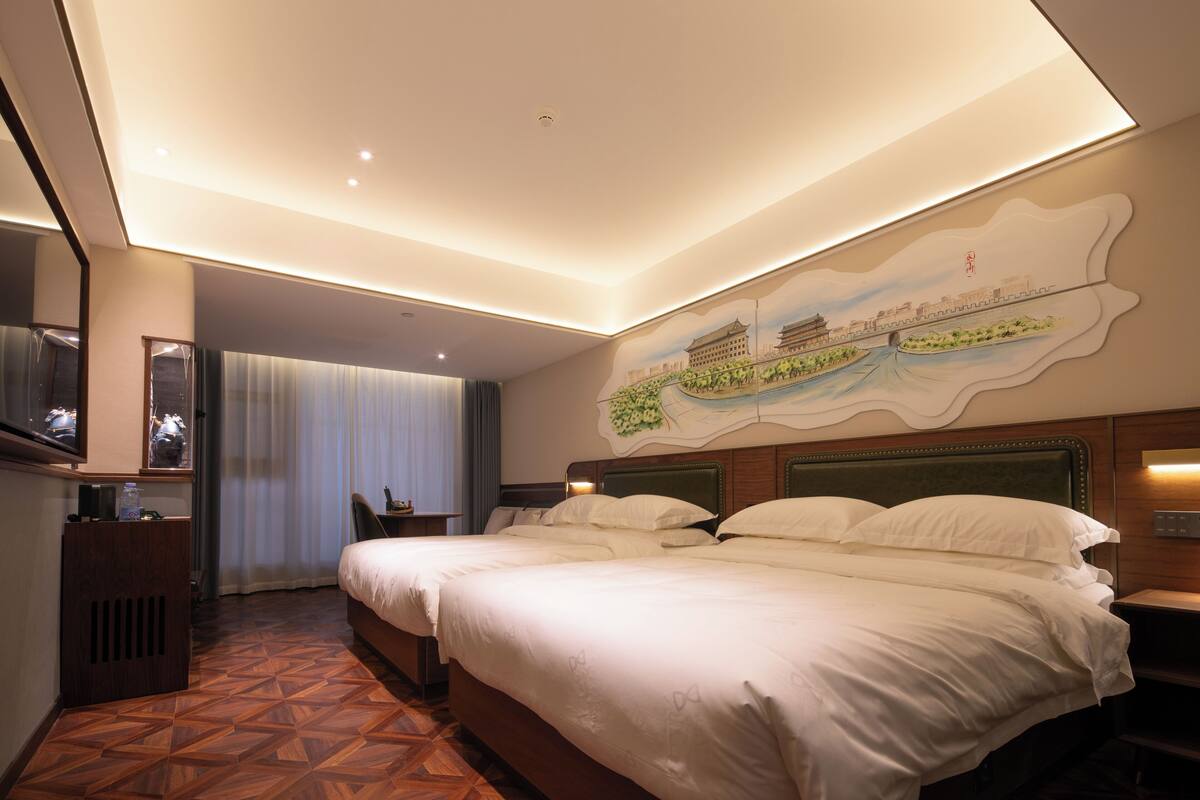 Ein Hotelzimmer mit zwei Betten, einem großen Spiegel, einem Flachbildfernseher und einem Wandgemälde.