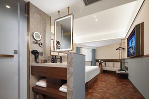 Une chambre d’hôtel moderne dotée d’un grand miroir, d’un lit, d’une télévision et d’une salle de bain comprenant un porte-serviettes et des articles de toilette.