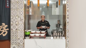 A person in a uniform holding bowls, with a kitchen counter displaying various utensils and containers.