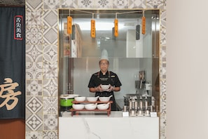A person in a uniform holding bowls, with a kitchen counter displaying various utensils and containers. - Nostalgia S Hotel  Xi'an Bell Tower (Xi'an)