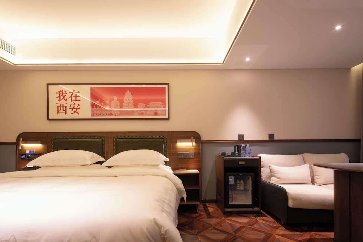 Ein Hotelzimmer mit Bett, Schreibtisch, Stuhl, Nachttisch und einem Wandbild.