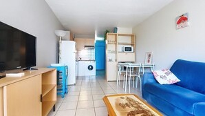 Un saló amb televisió, un sofà blau, una taula de centre i cuina al fons.