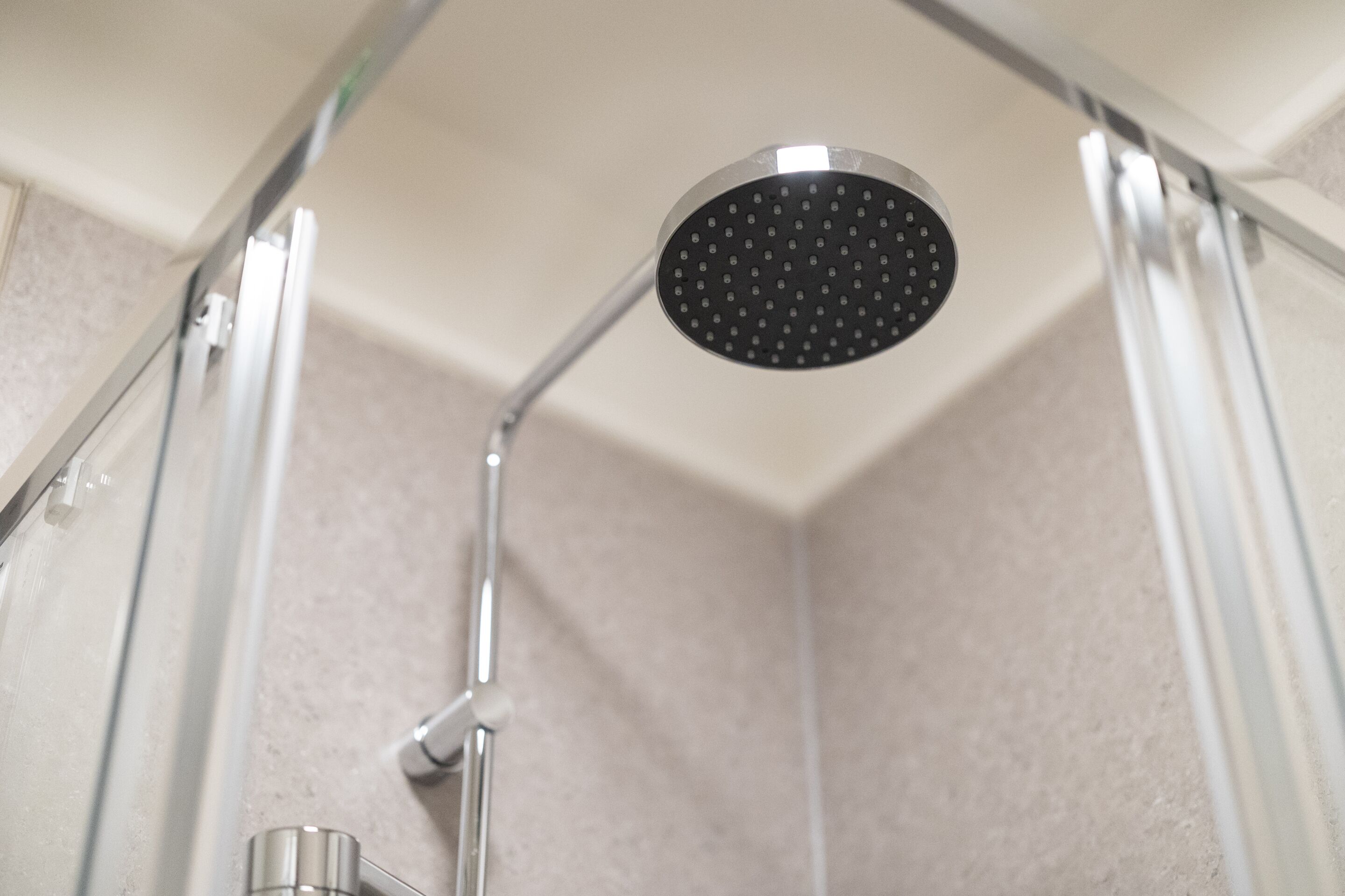 A showerhead in a bathroom with a tiled wall and a metal frame.