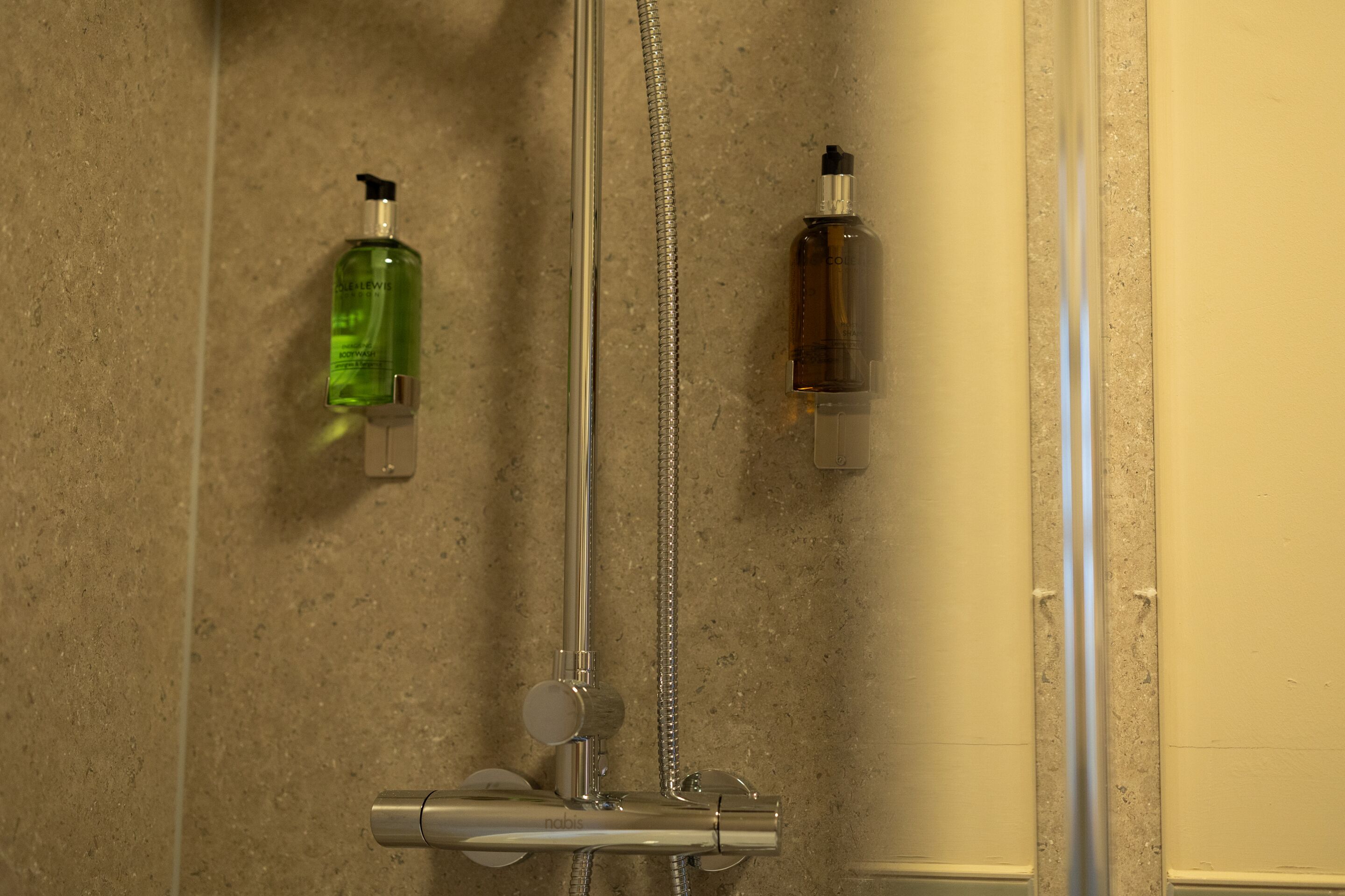 Un bagno con doccia, due flaconi di sapone liquido e un rubinetto.