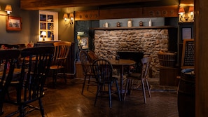 A cozy bar area with wooden furniture, a stone fireplace, and wall-mounted lighting. - The Slow & Easy (Northwich)