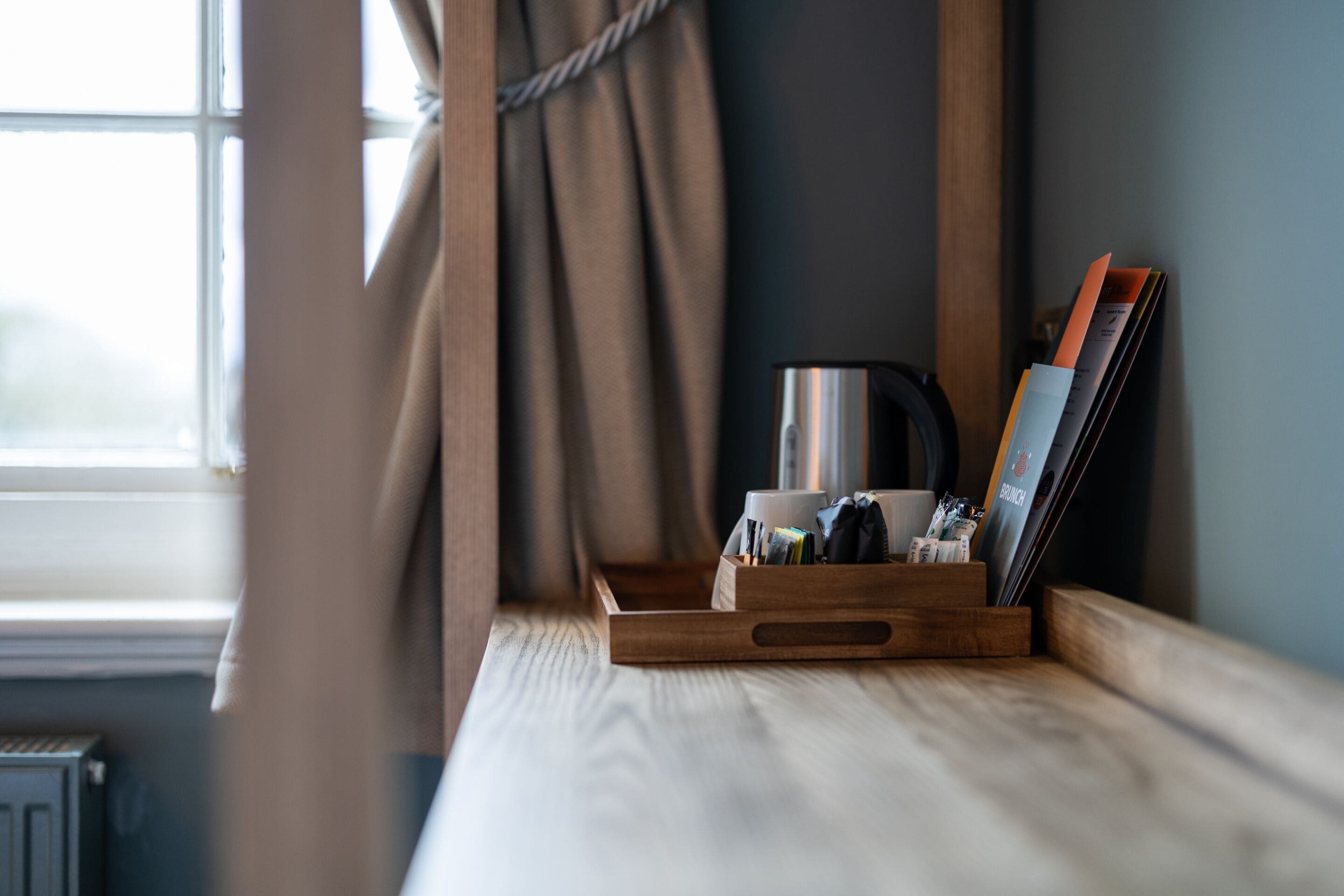 A wooden tray with a kettle, a cup, and a magazine holder on a window sill.