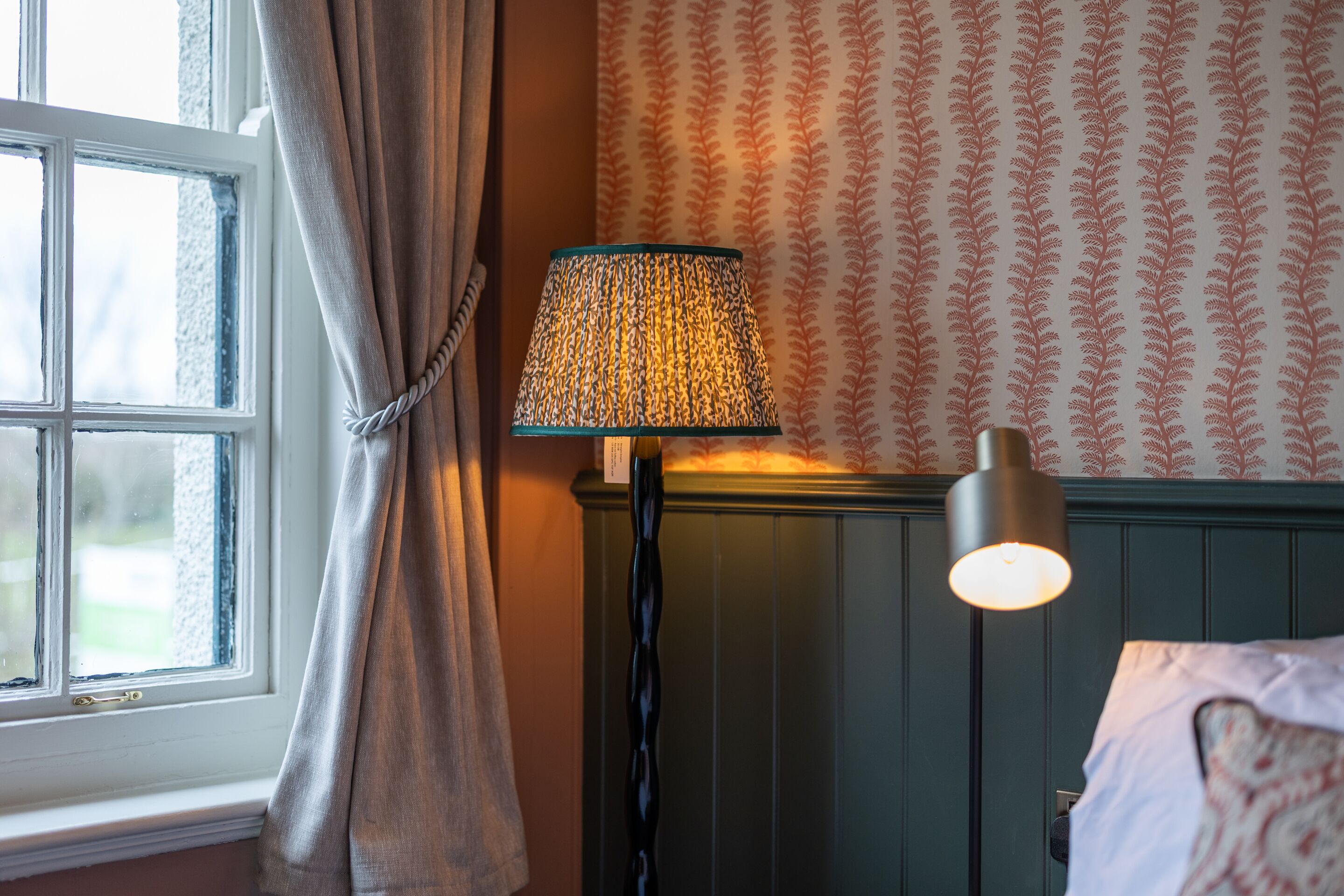 A room with a window, a lamp, and patterned wallpaper.