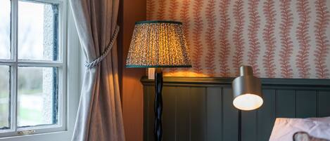 A room with a window, a lamp, and patterned wallpaper.