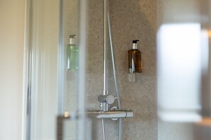 A shower with a glass door, a handheld showerhead, and two bottles of liquid soap on the wall. - The Slow & Easy (Northwich)