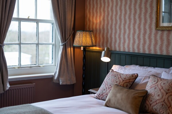 A hotel room with a bed, a lamp, a window with curtains, and patterned wallpaper. - The Slow & Easy (Northwich)