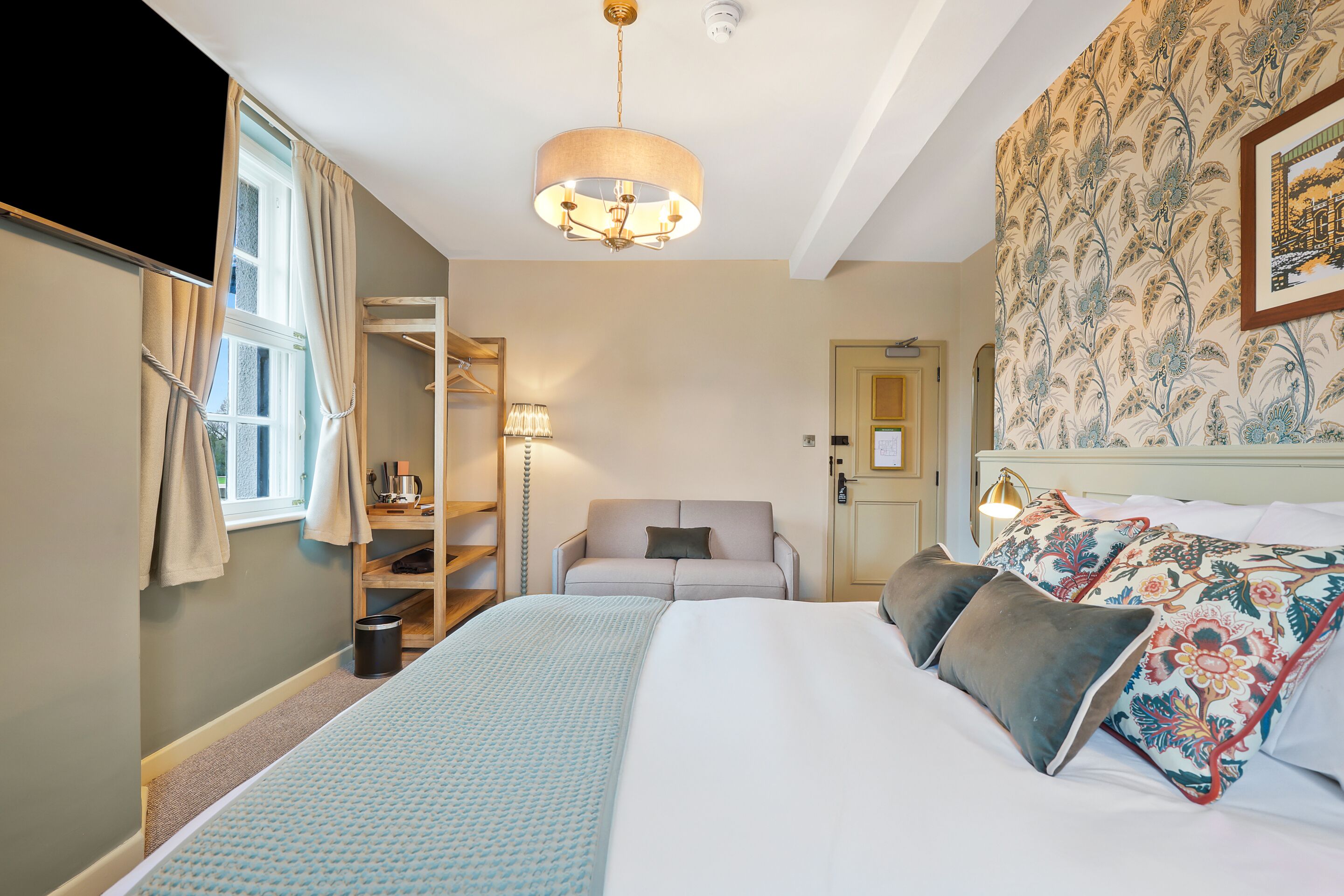 A hotel room with a bed, a sofa, a lamp, a wardrobe, and a window.