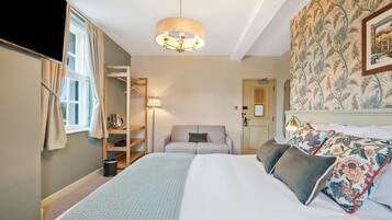 A hotel room with a bed, a sofa, a lamp, a wardrobe, and a window.
