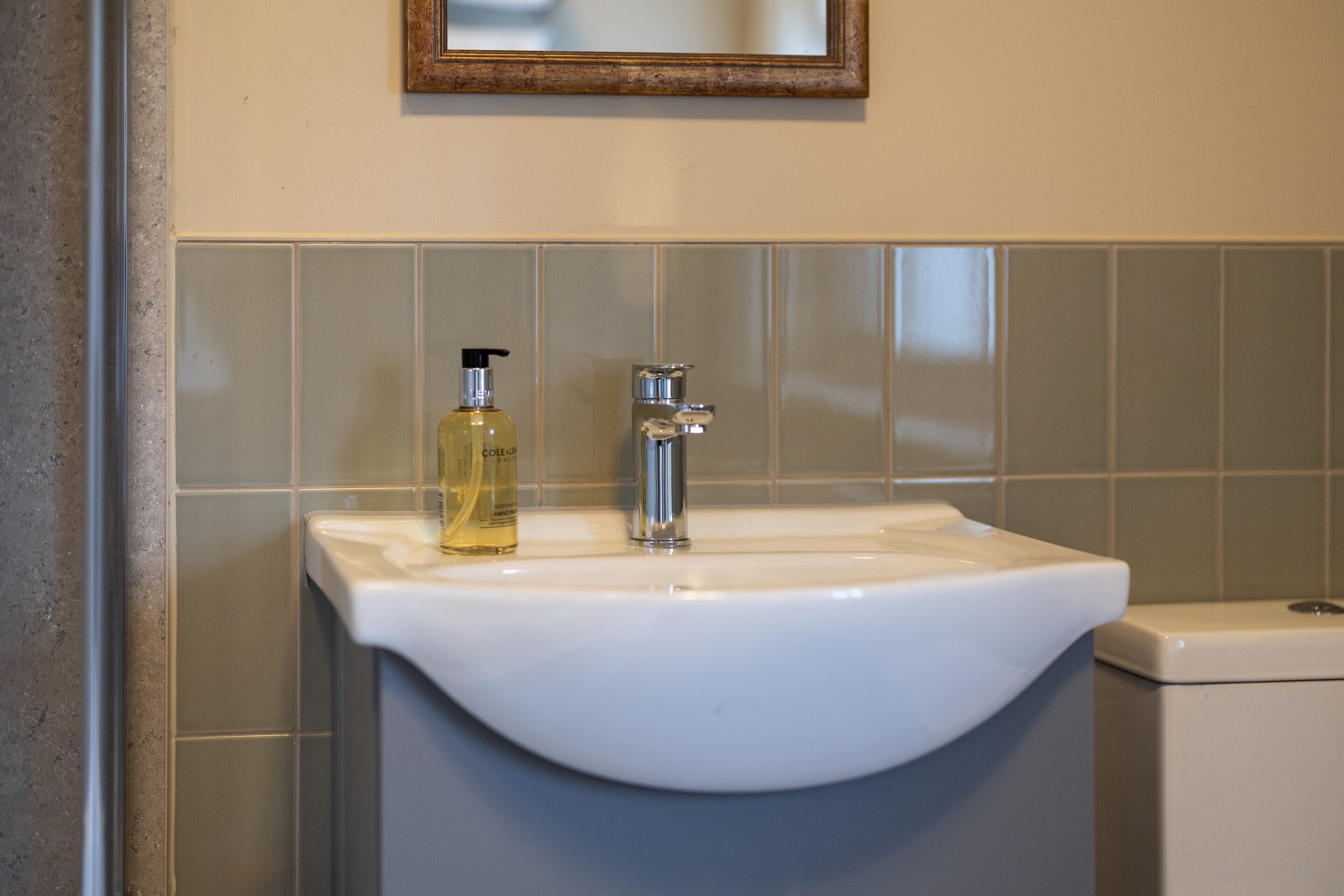 Een badkamer met een witte wastafel, een fles vloeibare zeep en een spiegel boven de wastafel.