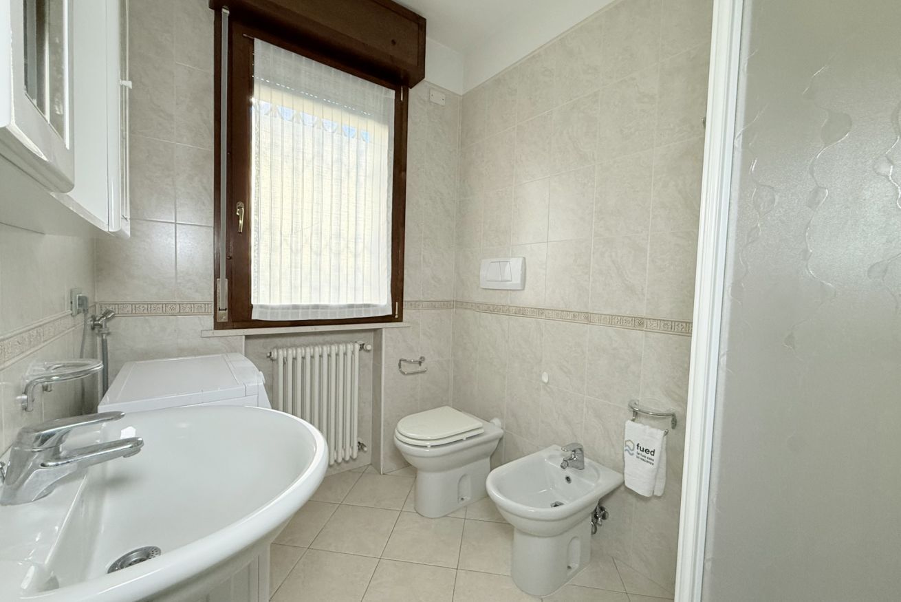 A bathroom with a sink, toilet, bidet, and a window with curtains.