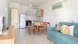 Een compacte leefruimte met een kitchenette, een eethoek en een bank met decoratieve kussens.