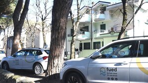 Twee geparkeerde auto's met 'fued' branding, een stenen muur en een gebouw met balkons op de achtergrond.