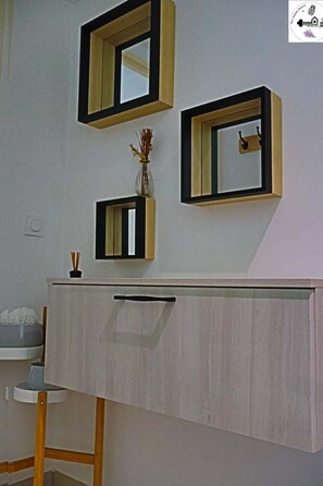 Un baño con tocador de madera, un espejo y un florero con flores secas.